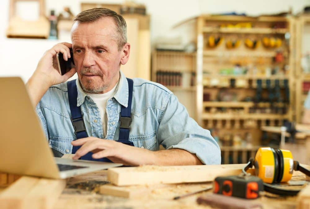 Business Owner On phone Looking At Laptop Figuring Out Should I Put My Company Into Voluntary Administration Or Liquidate It